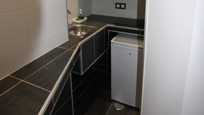 A compact kitchen with dark tiles, a small sink, and a white dishwasher. - Hostal MH Fuencarral (Madrid)