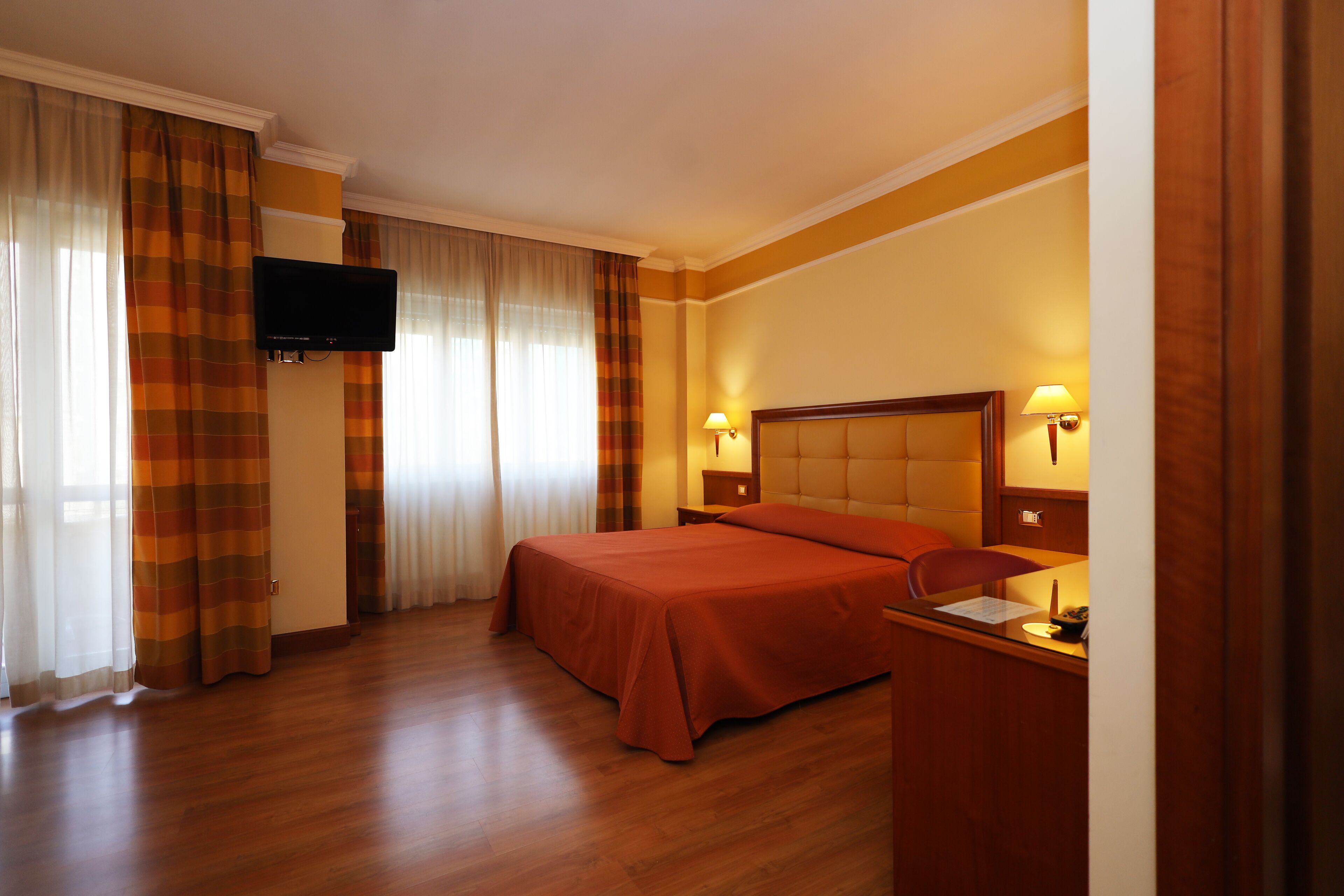 A hotel room with a bed, a desk, a chair, a television, and curtains.
