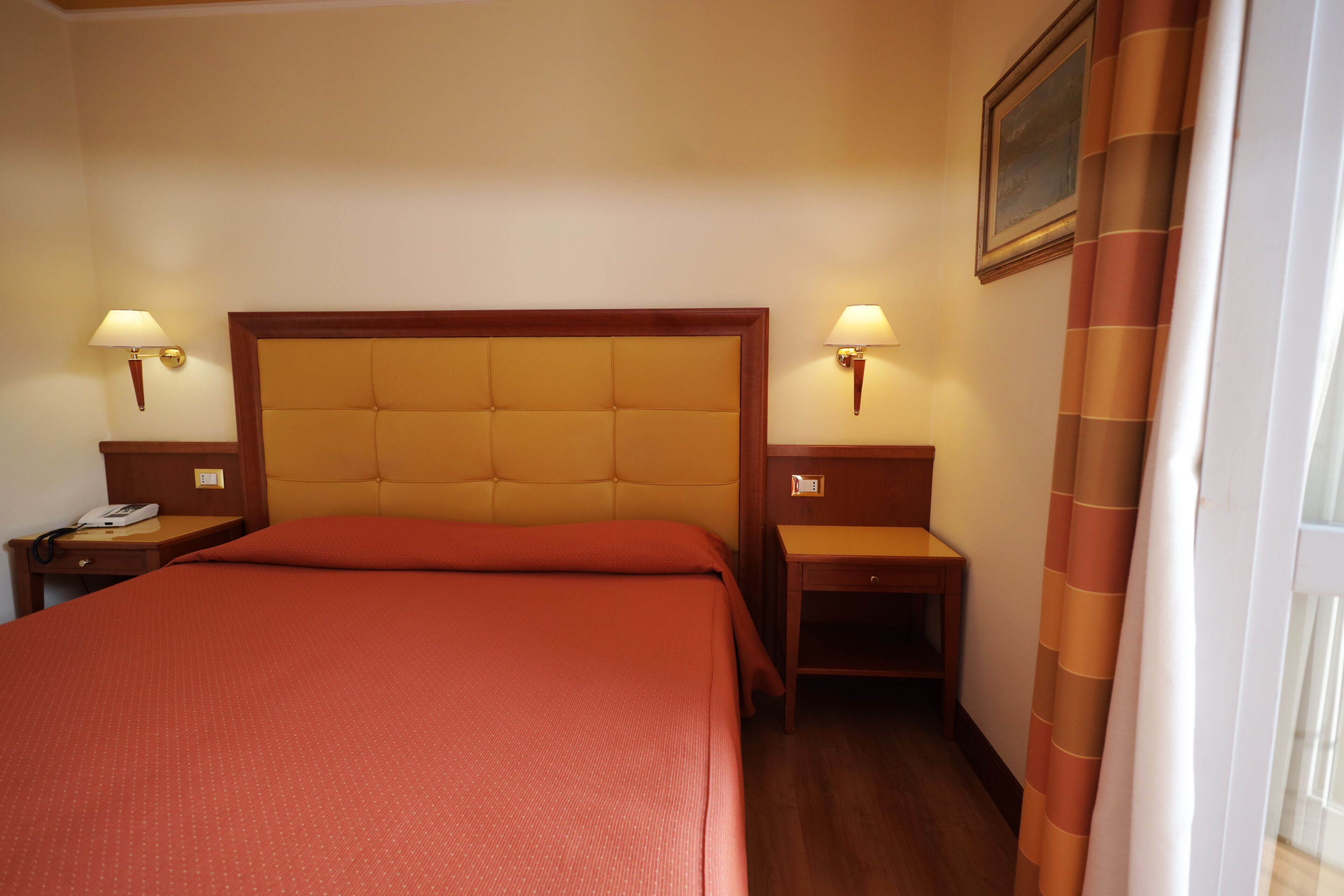 Ein Hotelzimmer mit einem großen Bett, zwei Nachttischen mit Lampen, einem hölzernen Kopfteil und einem Bild an der Wand.