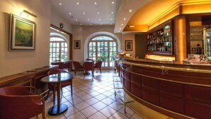 Een bar met een gebogen toonbank, diverse zitmogelijkheden zoals ronde tafels en stoelen, en een groot rondboogvenster dat natuurlijk licht binnenlaat.