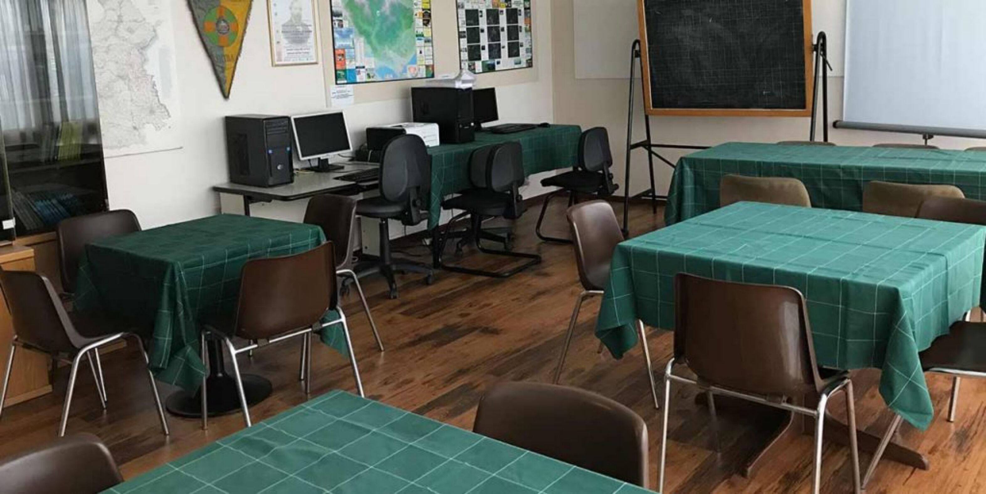 A classroom with green tables and chairs, computers, and a blackboard.