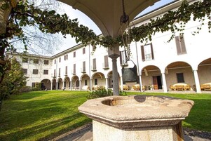 Un patio con una fuente de piedra, edificios blancos con arcos y mesas al aire libre.