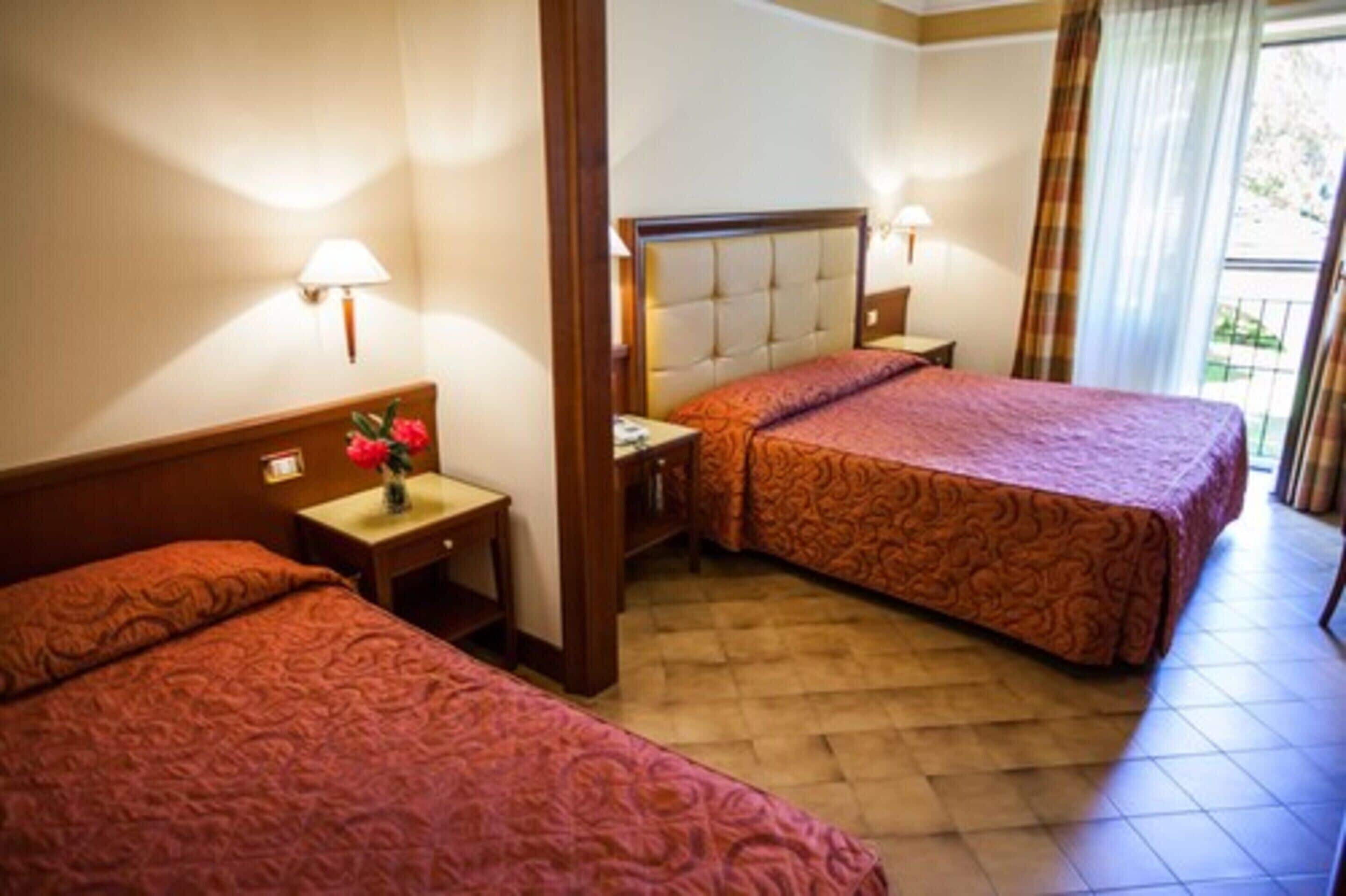 Habitación de hotel con dos camas, una mesita de noche con lámpara y una ventana con cortinas.