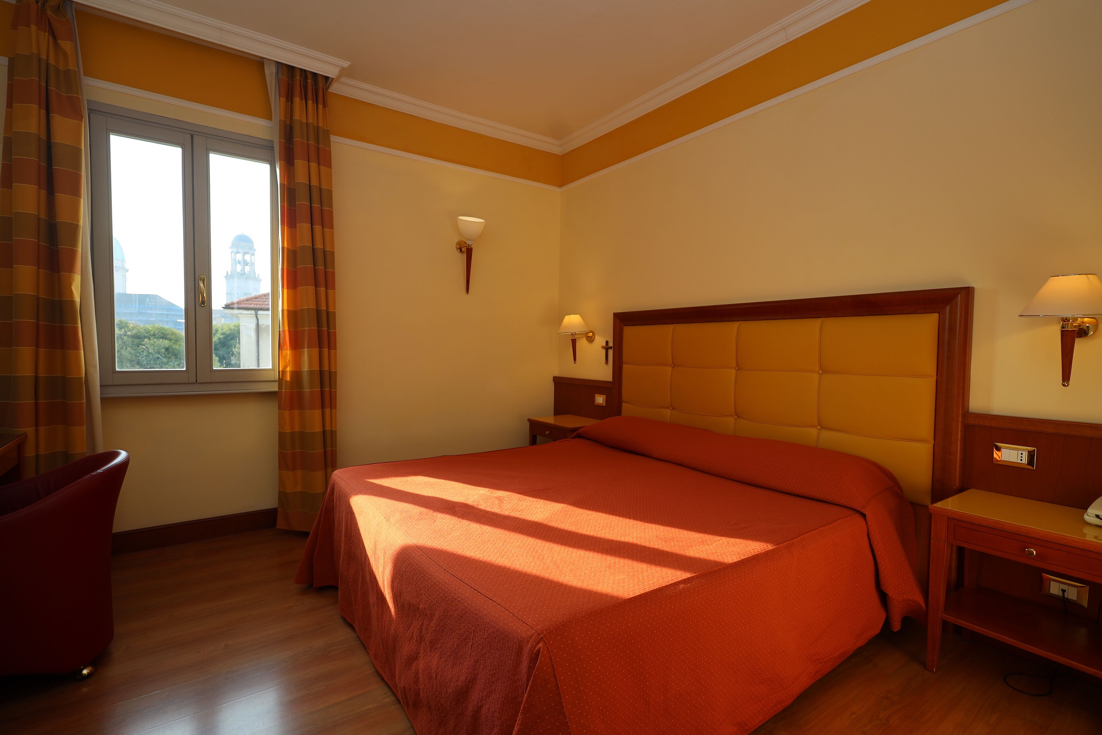 Ein Hotelzimmer mit einem großen Bett, zwei Nachttischen, einem Sessel und einem Fenster mit Vorhängen.