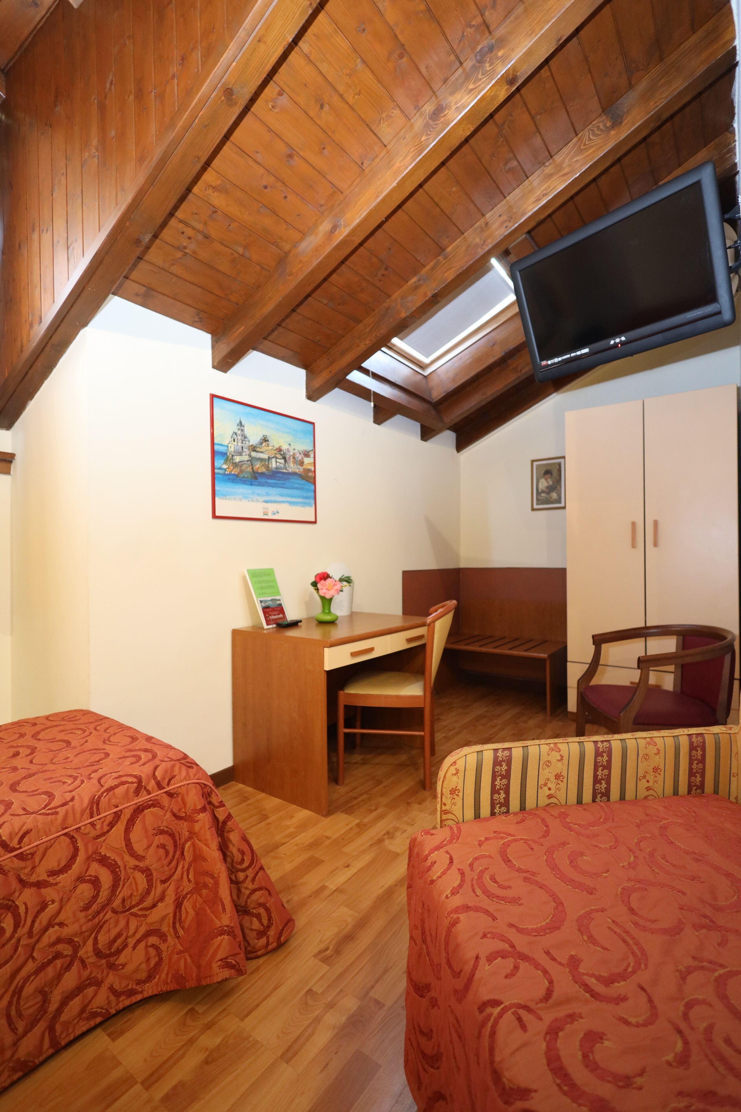 Una habitación acogedora con vigas de madera, un escritorio con silla, una cama y un televisor fijado a la pared.