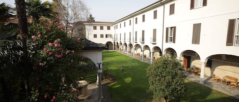A courtyard with a lawn, a palm tree, and a building with multiple windows and arches.