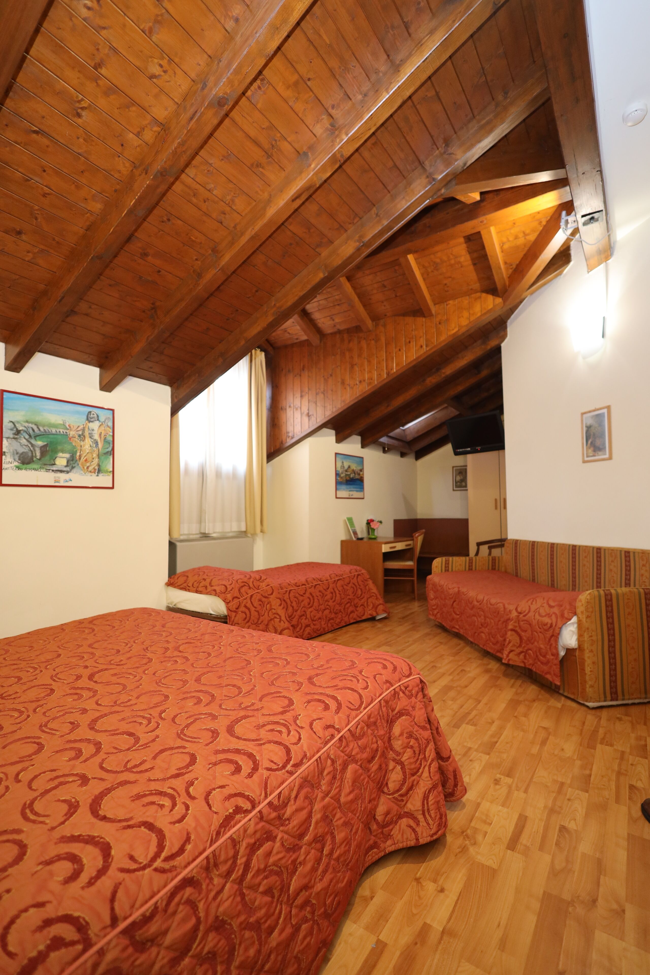 A cozy attic bedroom with two beds, wooden beams, and a desk.