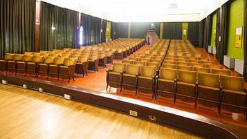 A large auditorium with rows of wooden chairs and a stage at the front.