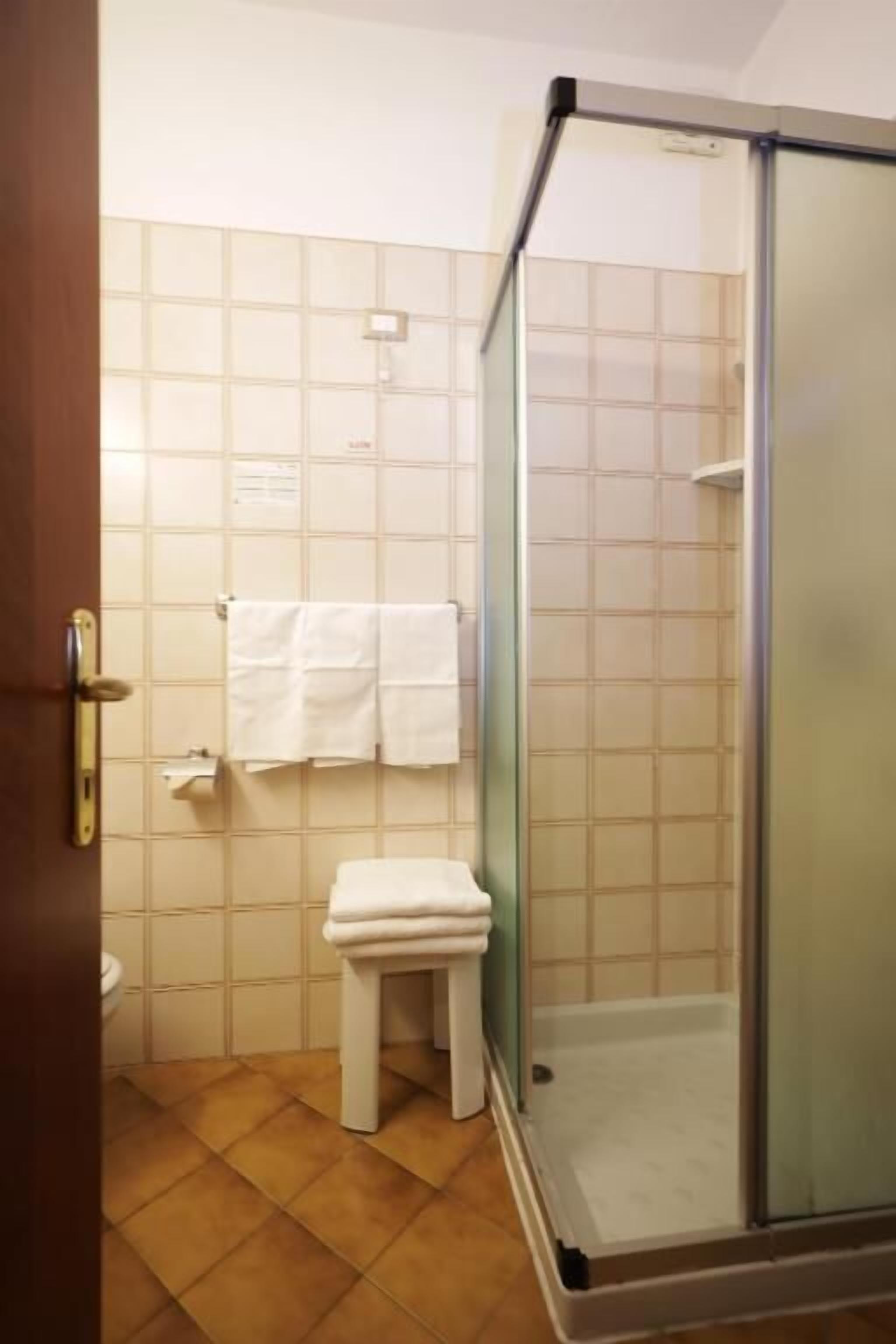 Un baño con cabina de ducha de vidrio, inodoro y un taburete pequeño.