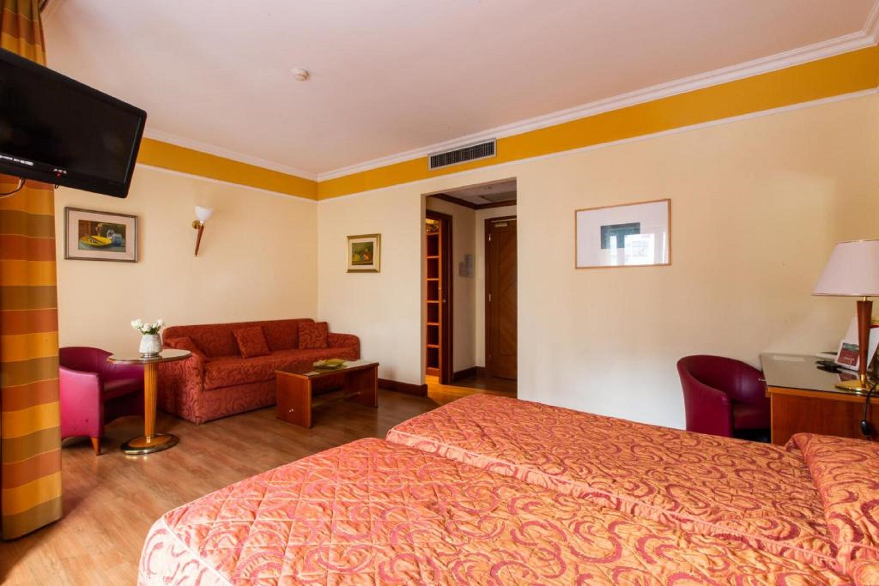 A hotel room with a bed, a sofa, a desk, and a television.