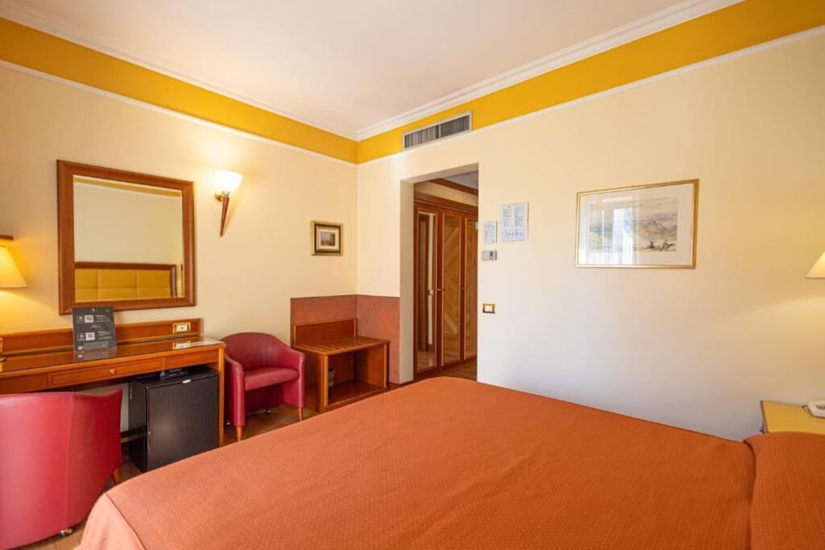 A hotel room with a bed, desk, chair, and a small kitchenette.