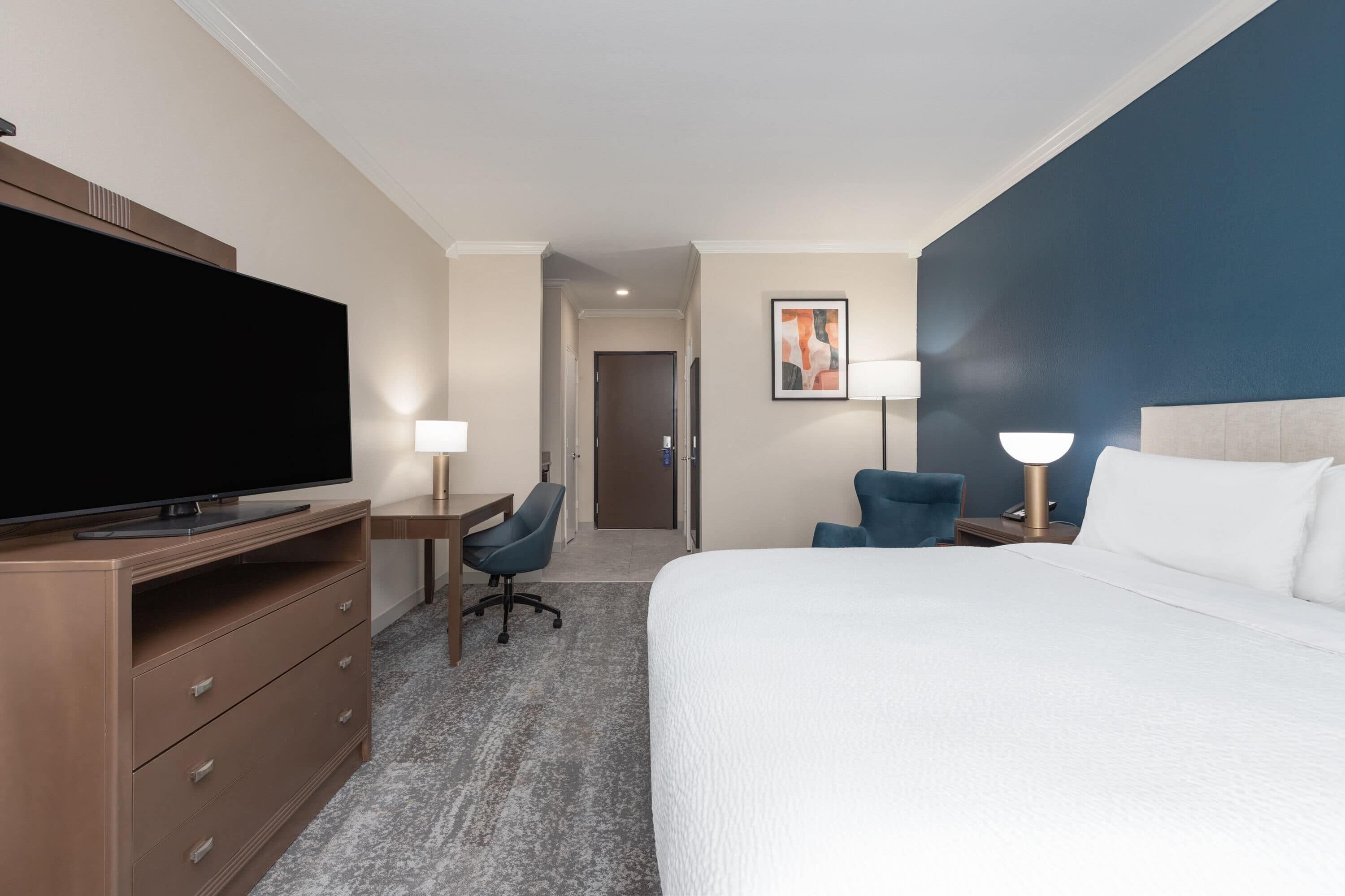A hotel room with a large bed, a desk with a chair, a television, and two bedside lamps.