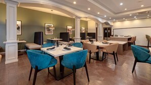 A modern dining area with teal chairs, white tables, and green walls. - Wyndham Lake Charles (Lake Charles)
