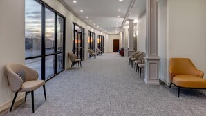 A hallway with large windows, carpeted flooring, and rows of chairs. - Wyndham Lake Charles (Lake Charles)