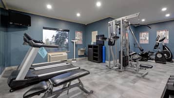 Un gimnasio con cinta de correr, banco de pesas y diversas máquinas de ejercicio.