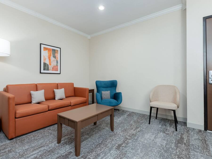 A room with a sofa, a blue armchair, a beige chair, a coffee machine, and a lamp.