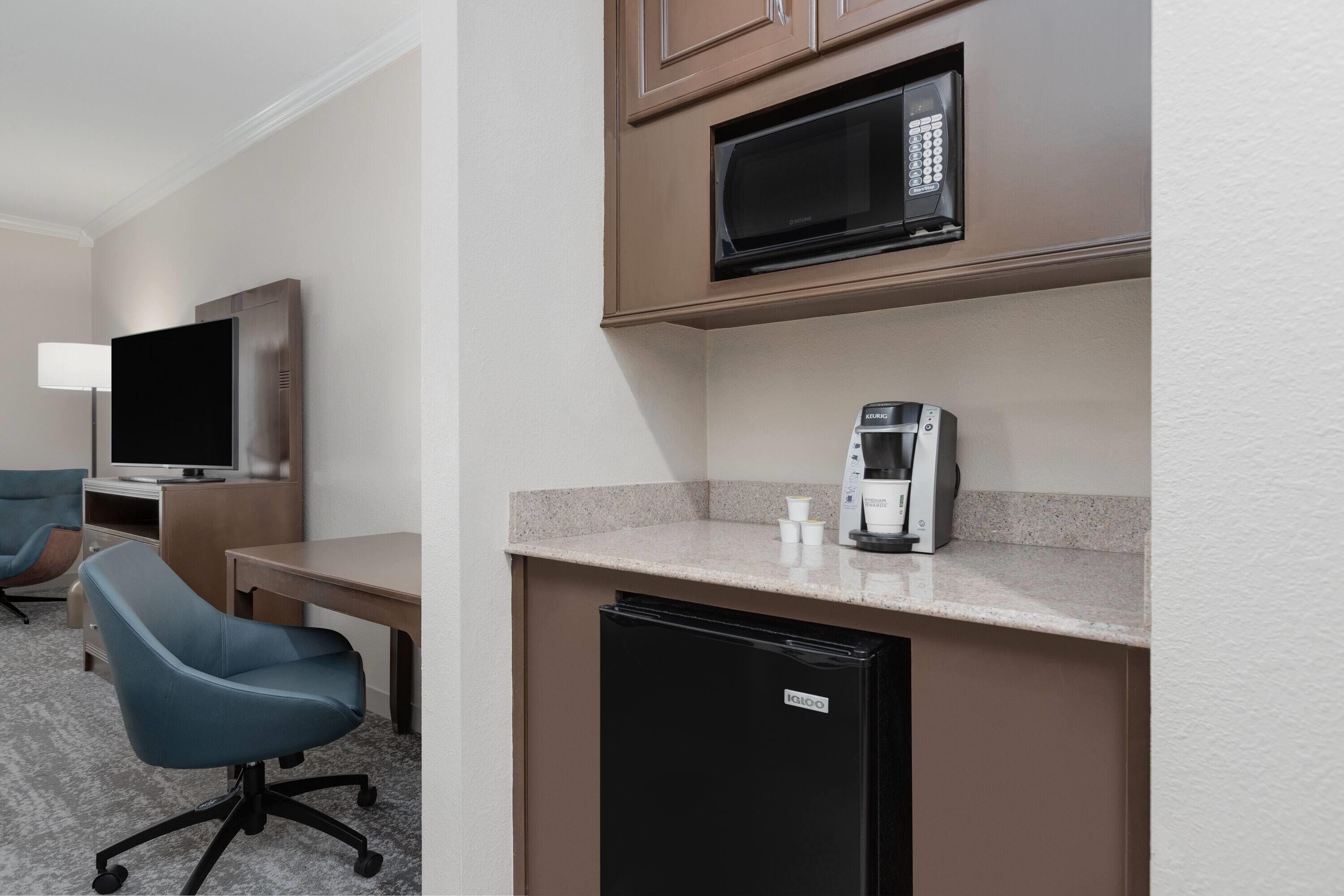 Une chambre d’hôtel compacte équipée d’une kitchenette, d’un téléviseur à écran plat, d’un fauteuil de bureau bleu et d’un petit réfrigérateur.