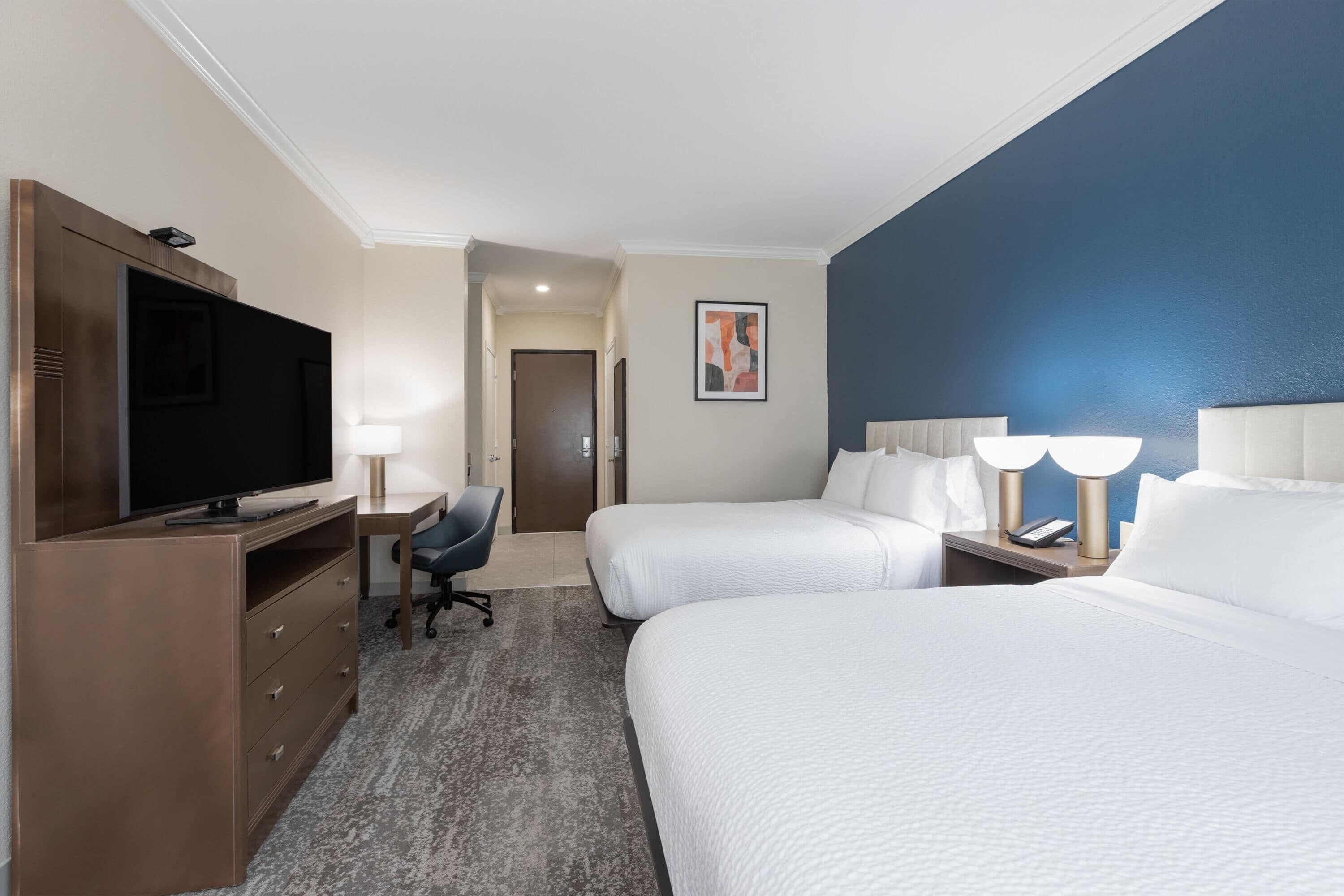 Una habitación de hotel con dos camas, televisor, escritorio y silla.