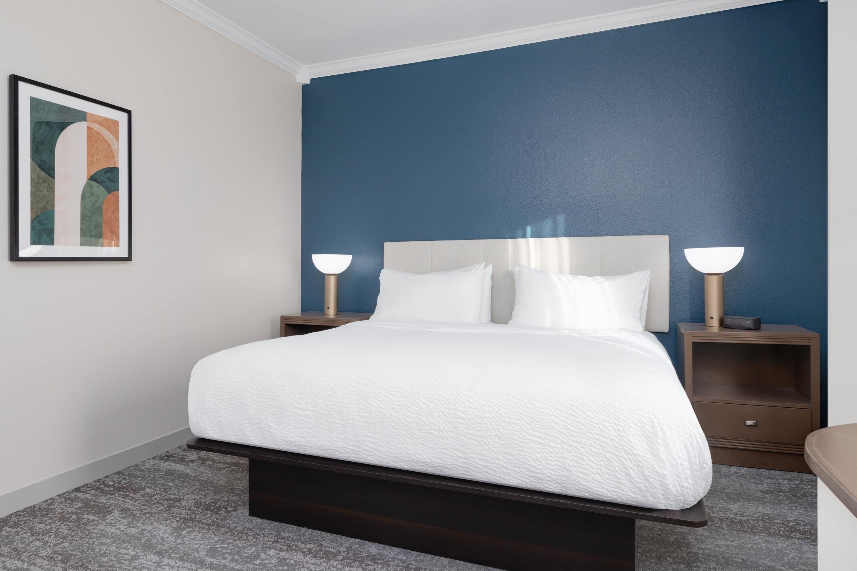 A neatly made bed with white linens, a dark headboard, and two bedside tables with lamps.