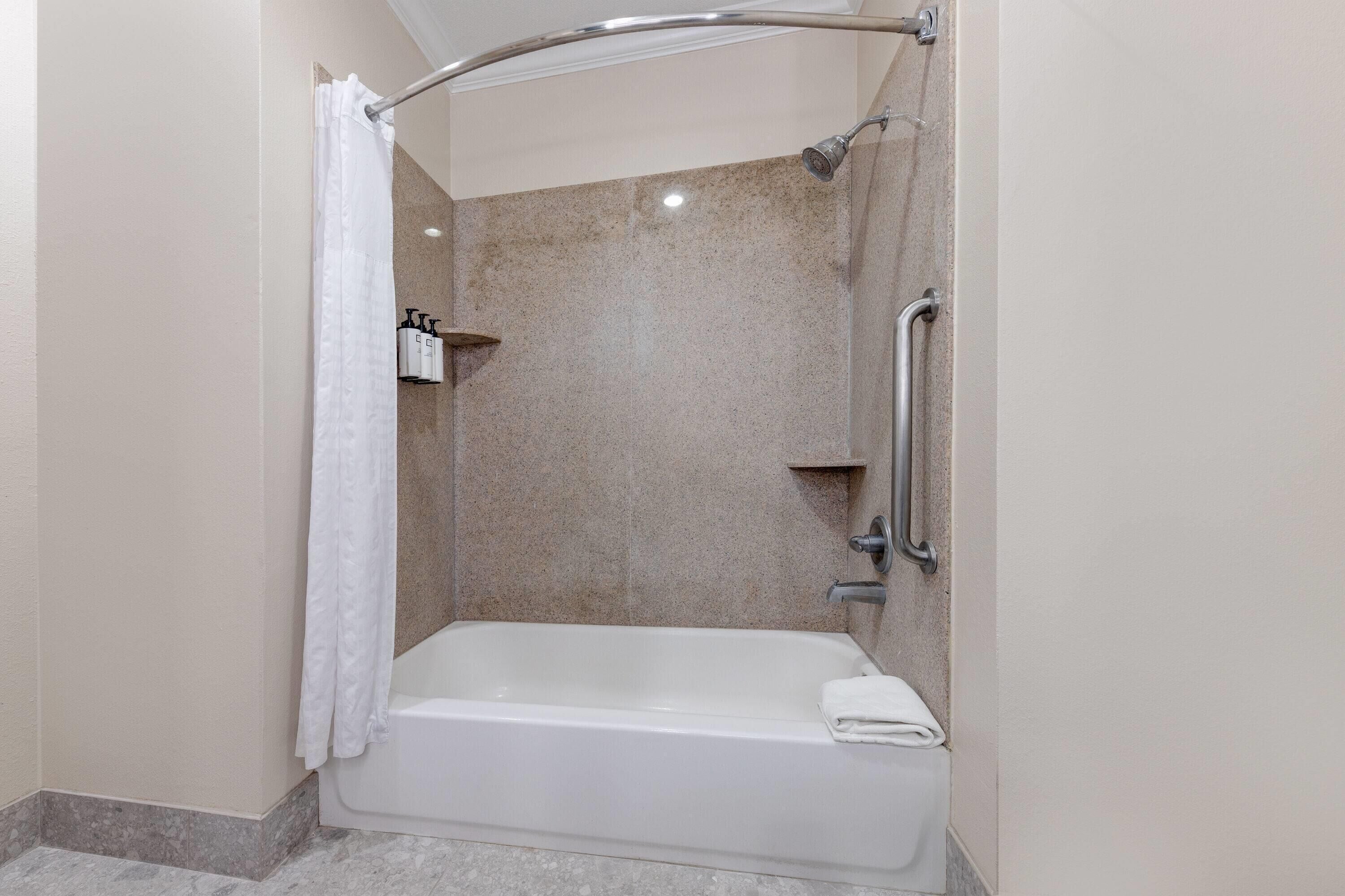 A modern bathroom with a walk-in shower, a bathtub, and a handrail.