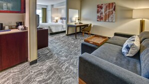 A hotel room with a gray sofa, a wooden side table, a desk with a chair, a bed, and a TV. - Springhill Suites by Marriott New Bern (New Bern)