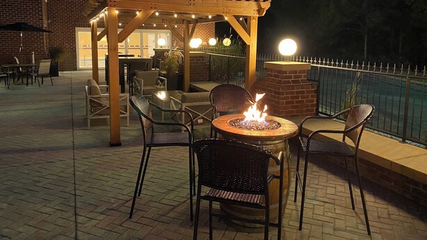 An outdoor patio area with a fire pit, seating, and a pergola with string lights. - Springhill Suites by Marriott New Bern (New Bern)