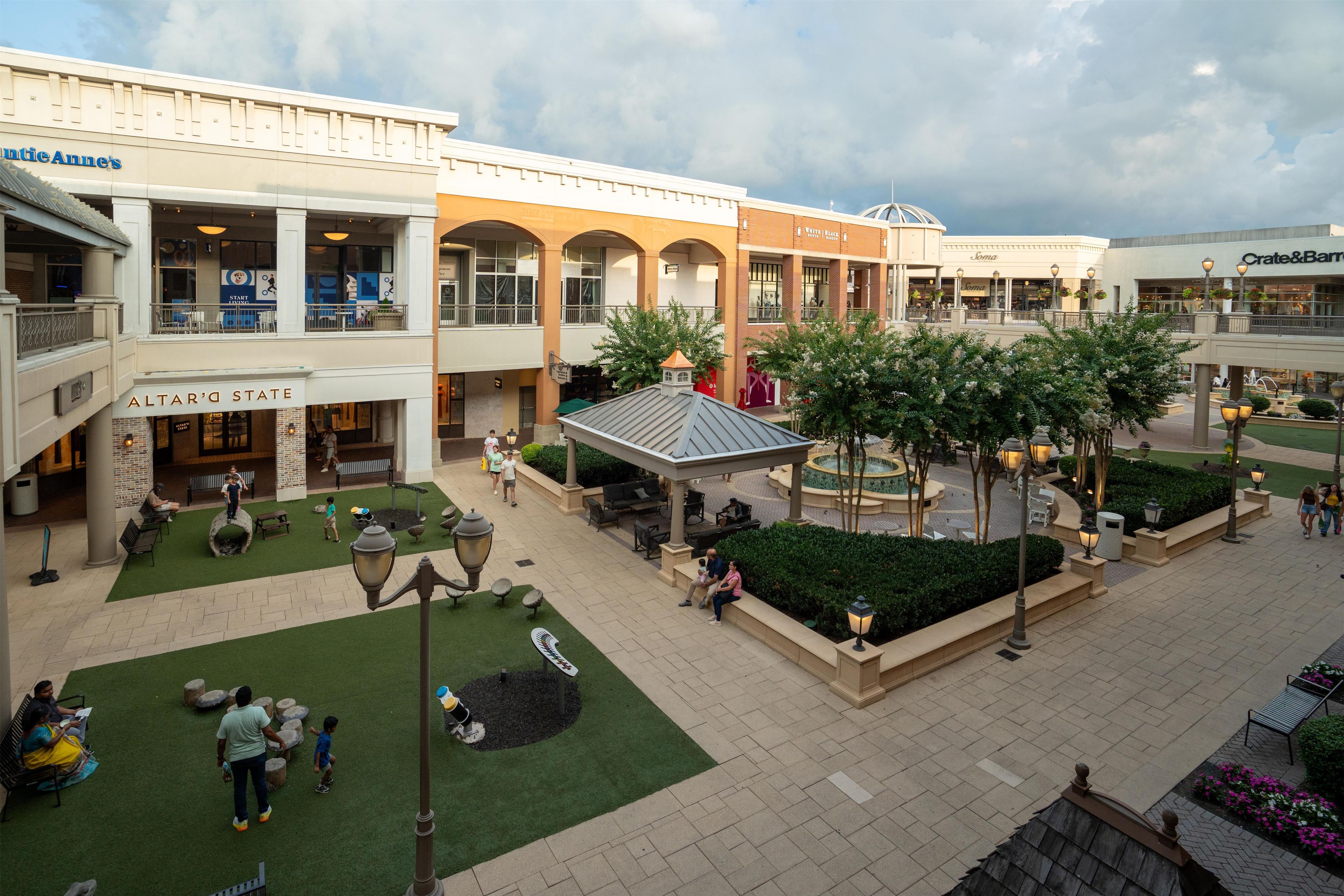 A shopping mall with multiple levels, outdoor seating areas, and a central fountain.