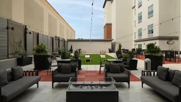 An outdoor seating area with sofas and tables, a small lawn, and a building in the background.