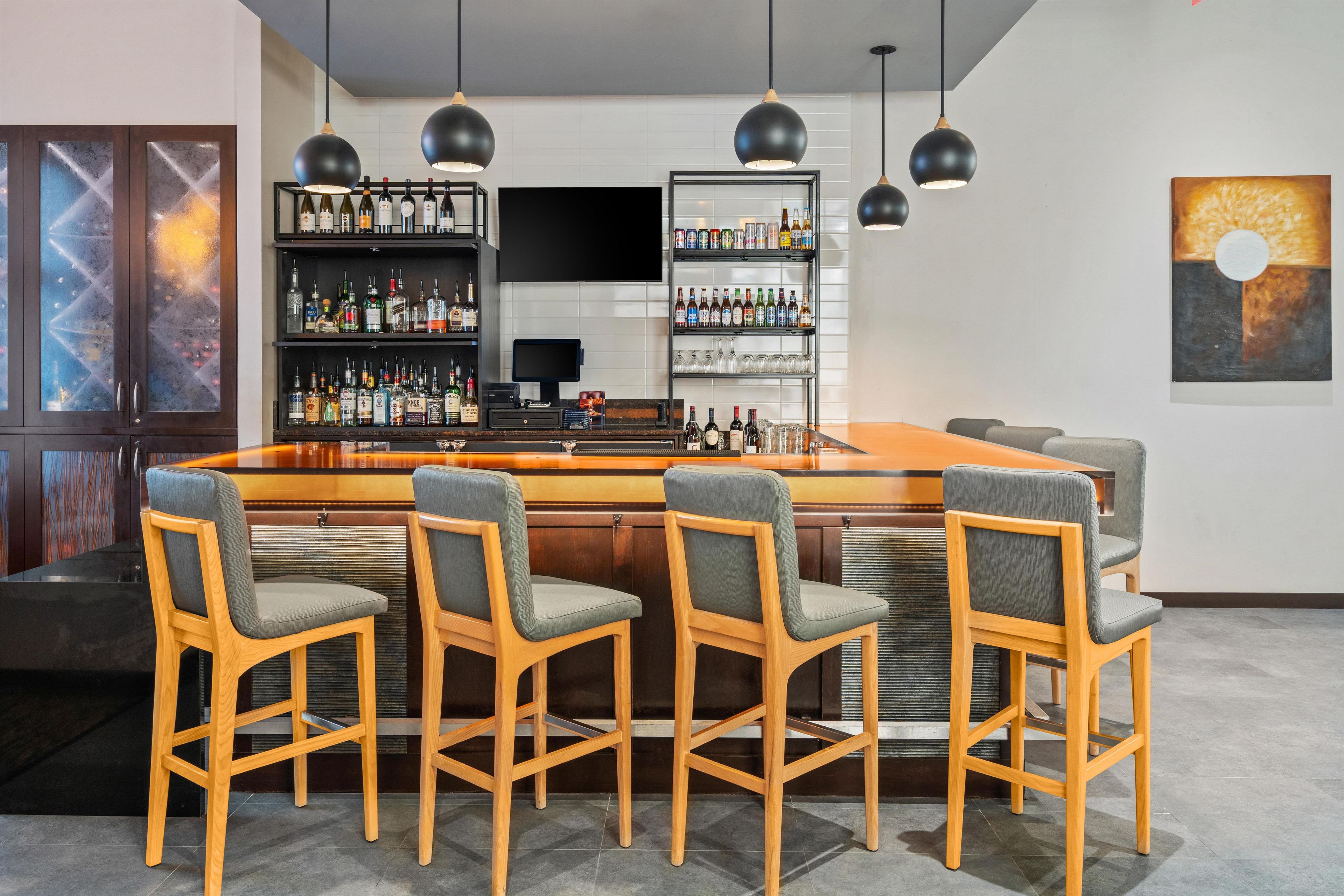 A bar area with a long counter, multiple stools, and shelves stocked with bottles.
