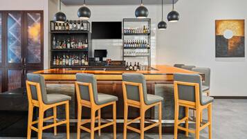 A bar area with a long counter, multiple stools, and shelves stocked with bottles.