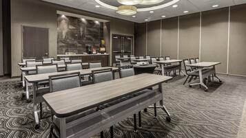 A conference room with multiple tables and chairs, a large screen, and a projector.