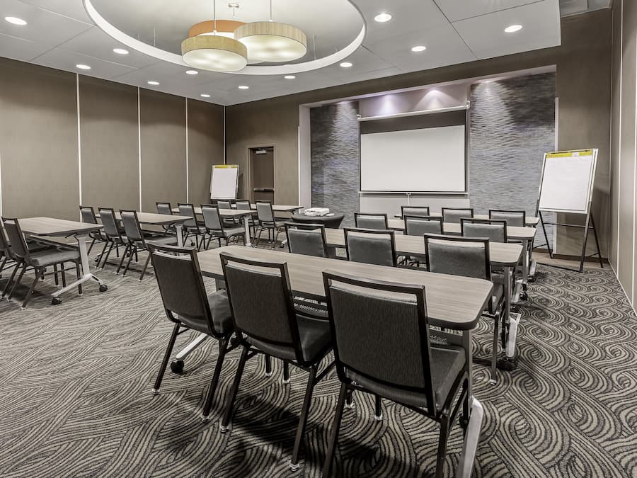 A conference room with multiple tables and chairs, a whiteboard, and a projector screen.