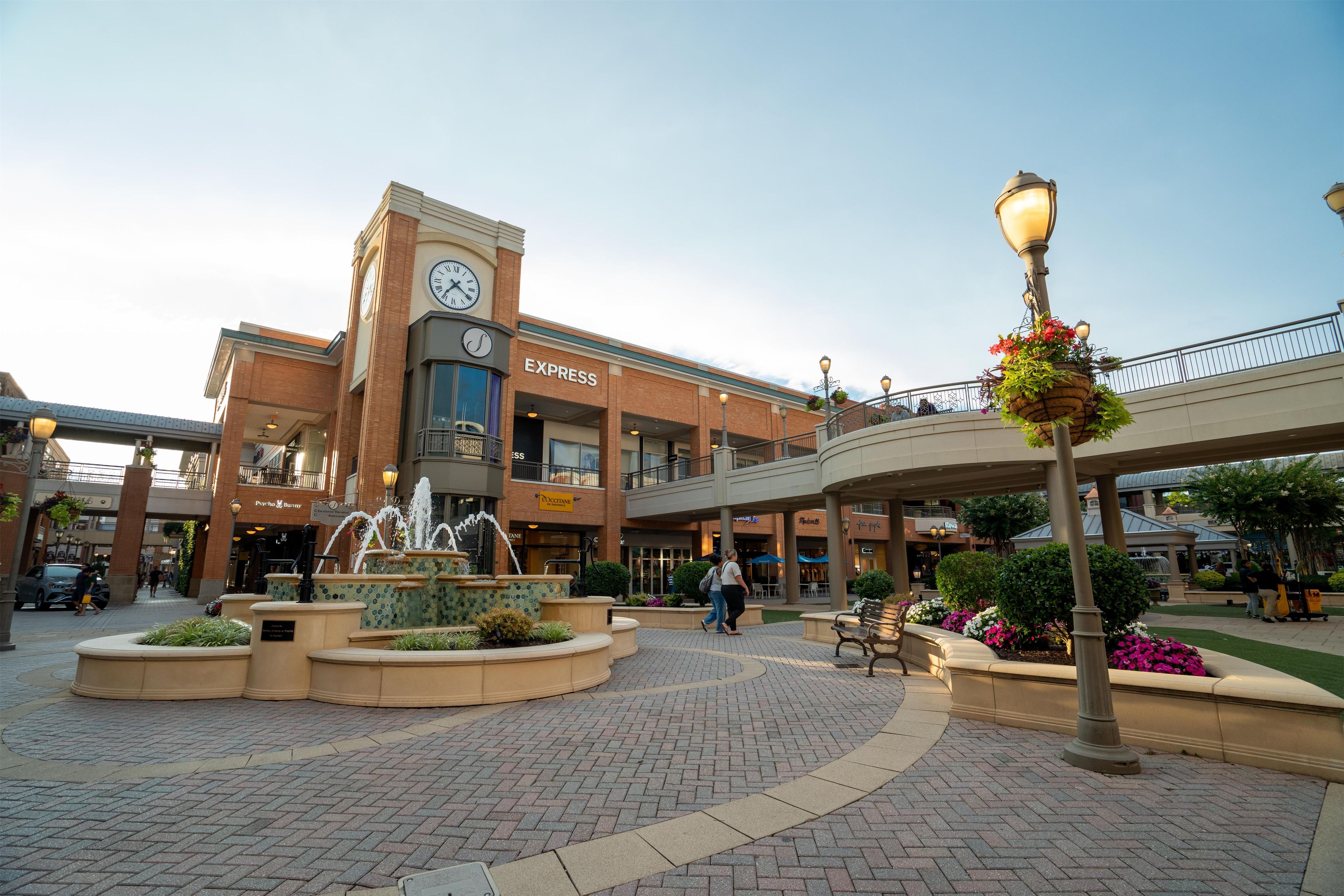 A shopping mall with a central fountain, a clock tower, and various stores including Express.