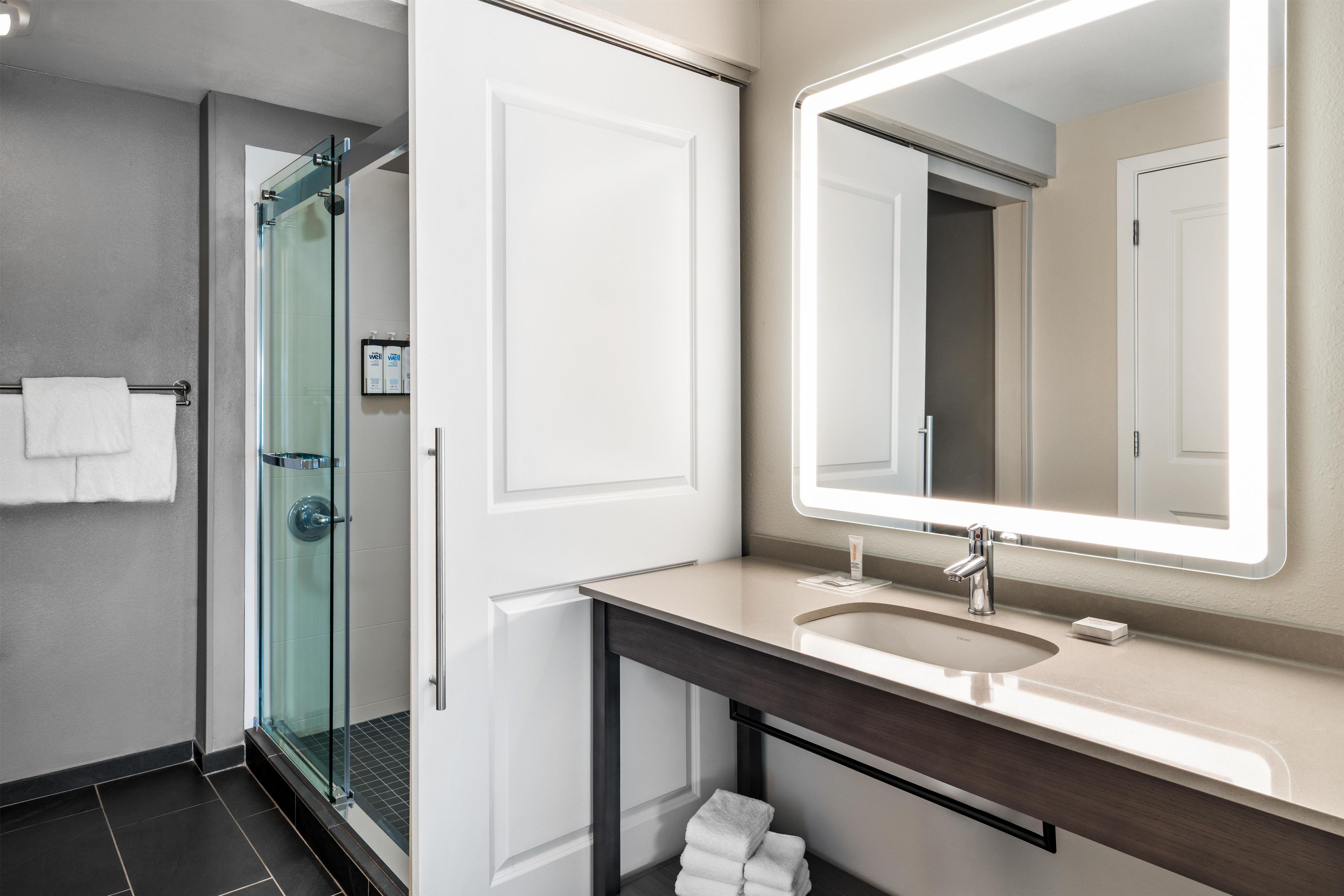 A modern bathroom with a glass shower enclosure, a vanity with a large mirror, and a sink.