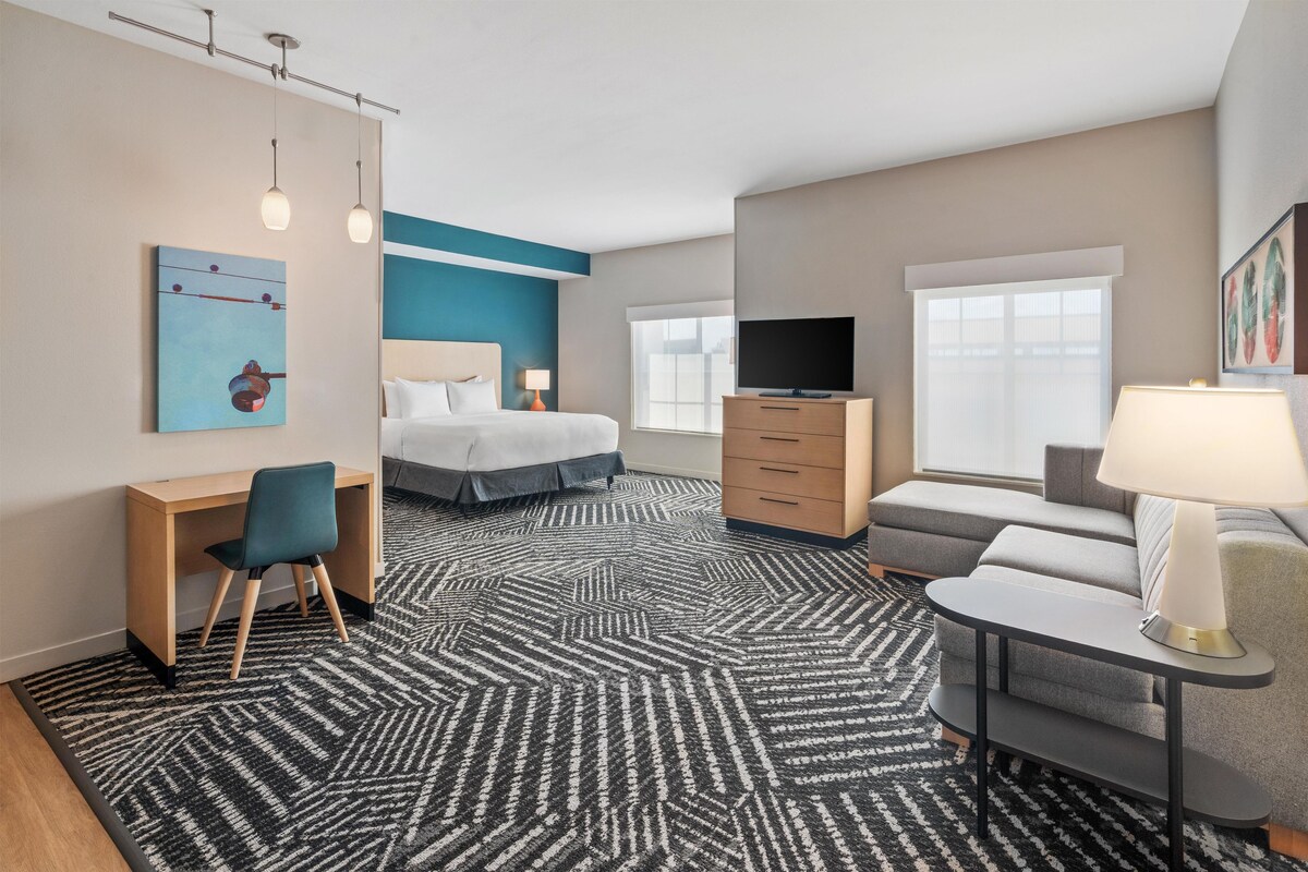 Een hotelkamer met een bed, bureau, stoel, televisie, bank en een kamerbreed tapijt met dessin.