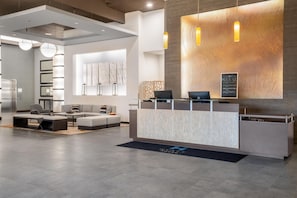 Un espace d’accueil moderne avec un comptoir en marbre, des sièges et une grande œuvre d’art accrochée au mur.