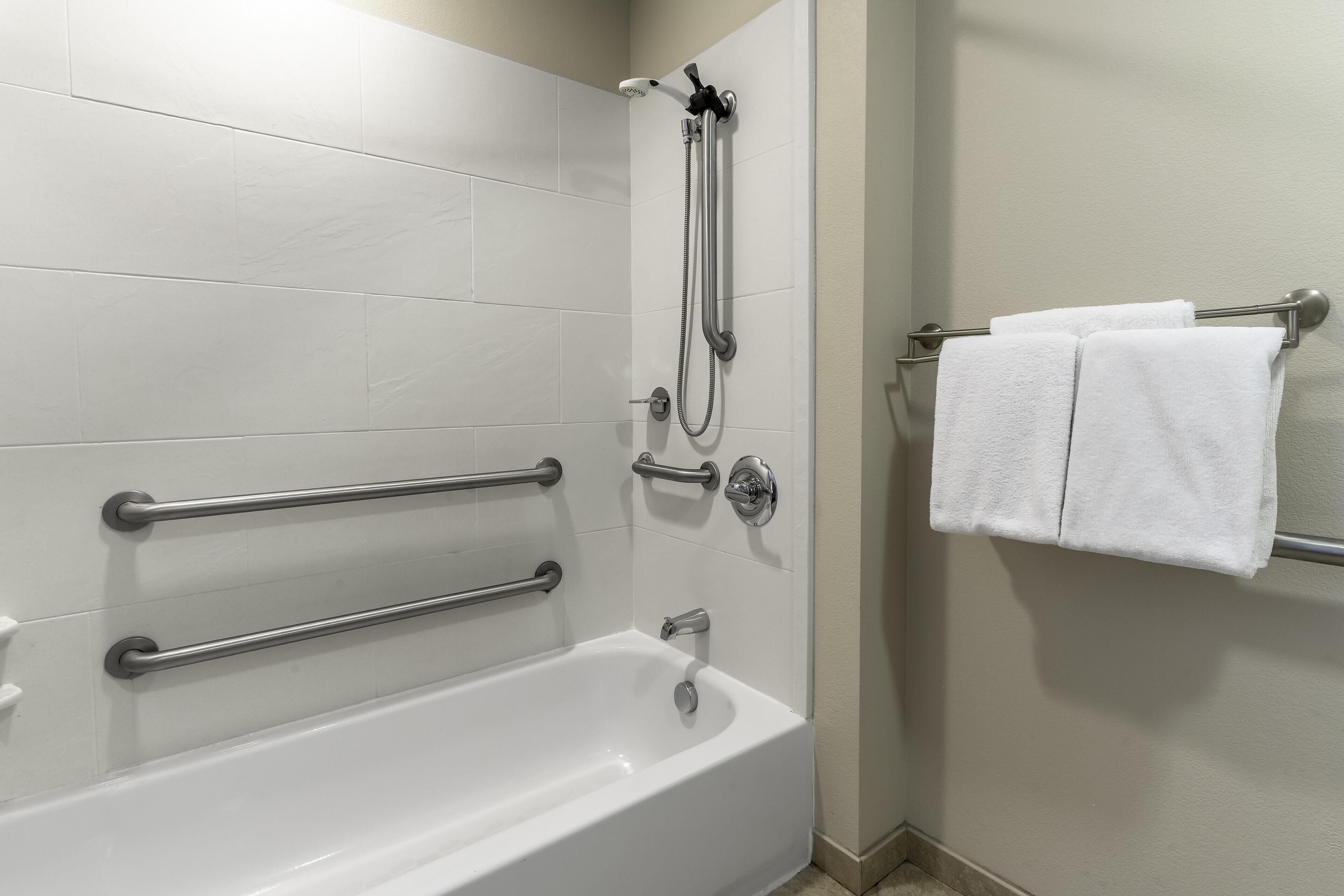 A bathroom with a white bathtub, grab bars, a shower head, and a towel rack with two towels.