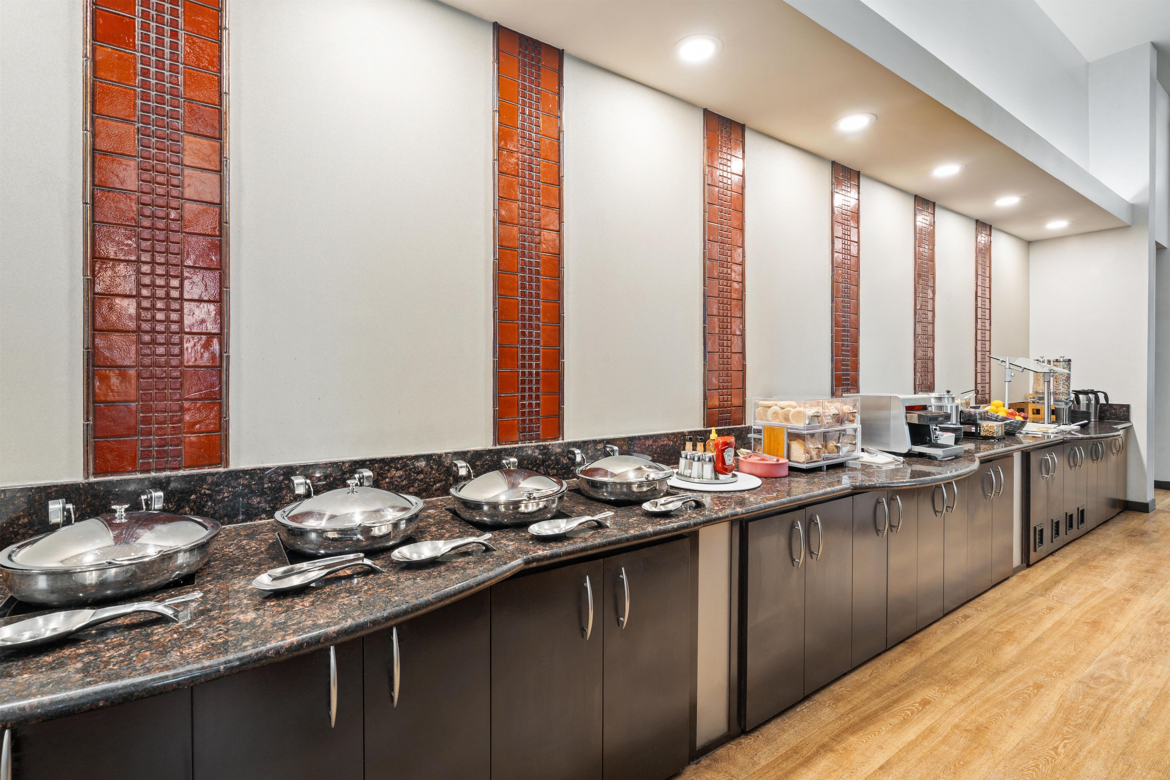 A long kitchen counter with various food service items, a coffee machine, and a fruit bowl.