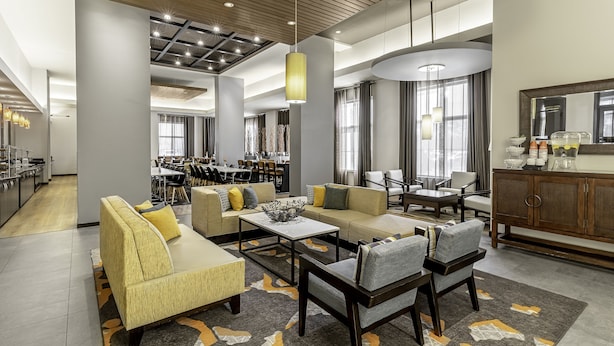 Un moderno vestíbulo de hotel con zona de comedor, sofás y una cocina al fondo.