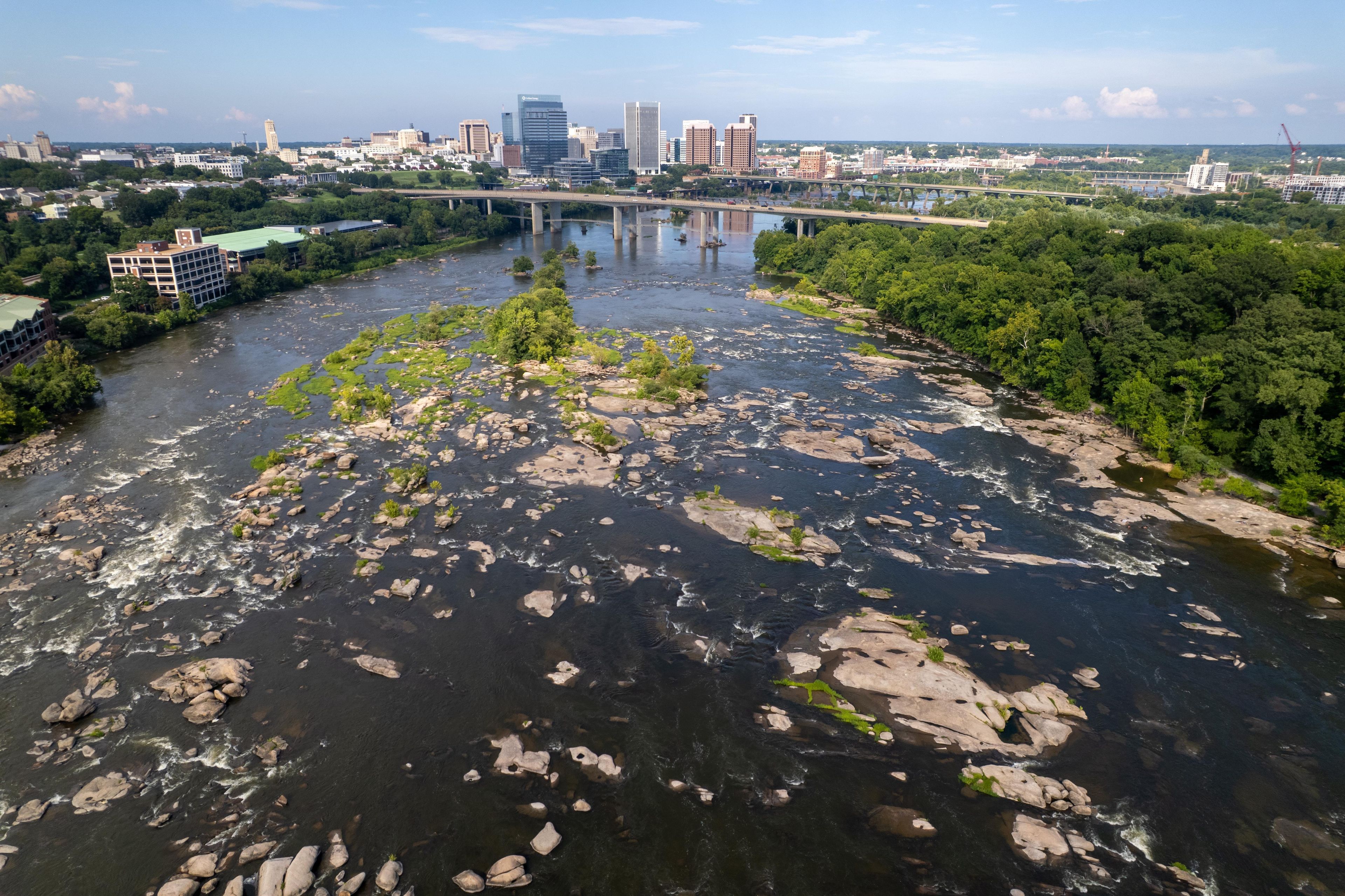 A river with rocks and greenery, a bridge, and a city skyline in the background.