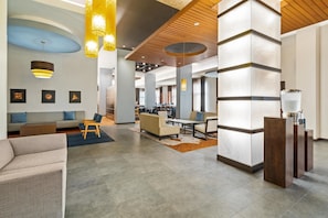 Un hall d’entrée spacieux au design moderne, comprenant un espace détente avec des canapés et des fauteuils, un comptoir d’accueil et un grand espace ouvert doté d’un plafond haut et de poutres en bois.