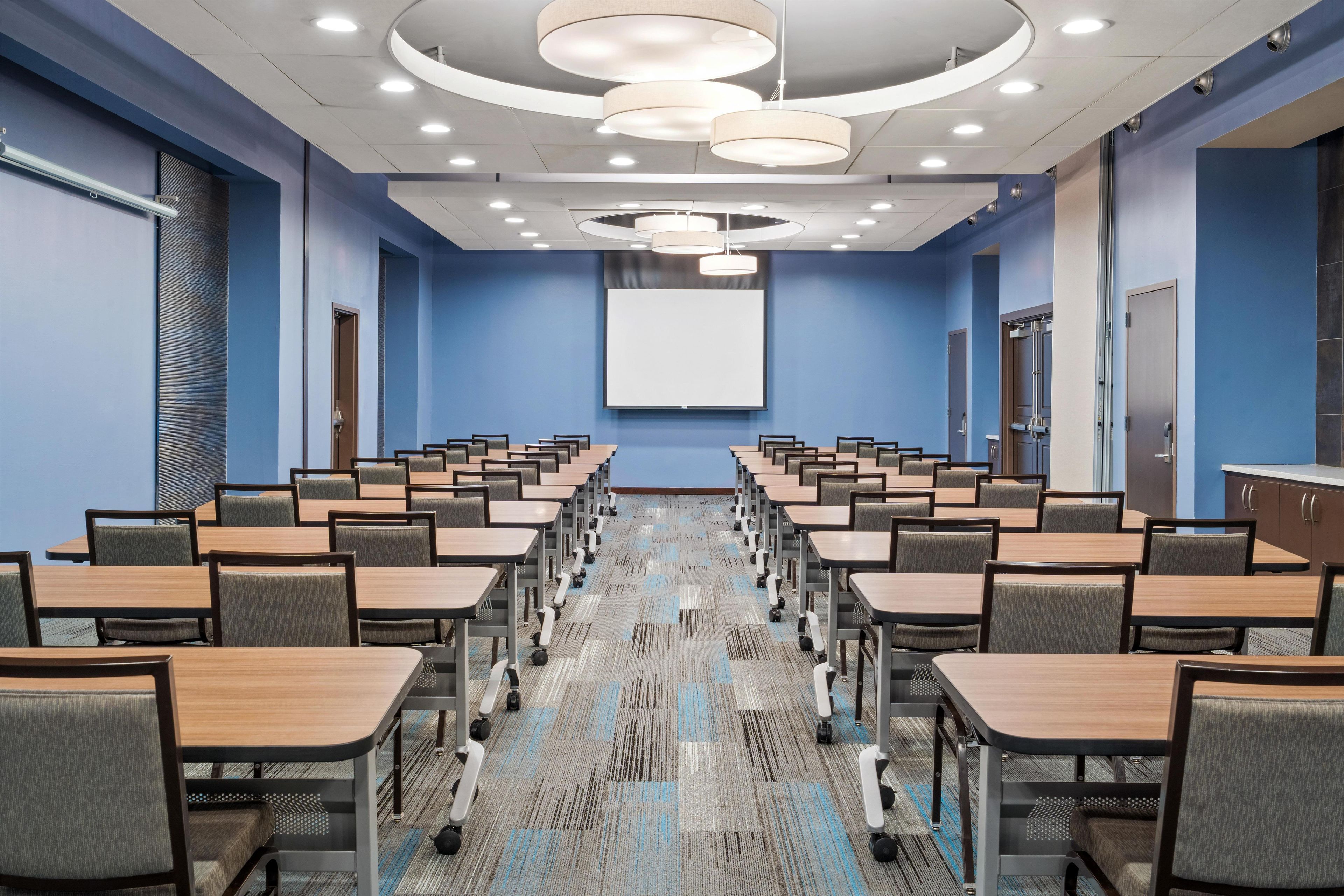A conference room with a long table, chairs, a projector screen, and a carpeted floor.
