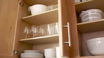 A wooden cabinet with shelves containing white dishes, glasses, and a measuring cup.