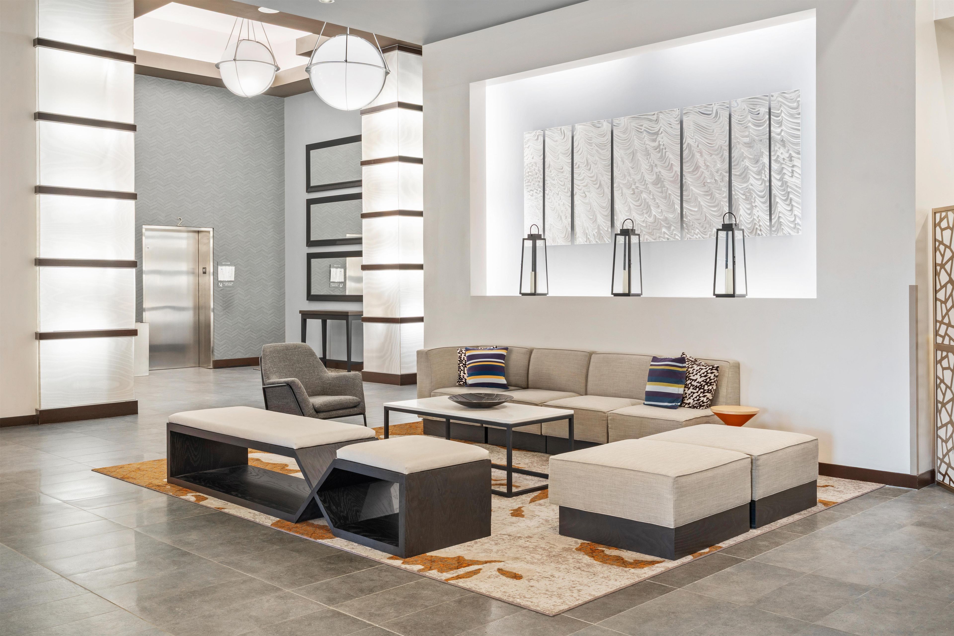 A modern living room with a sofa, ottoman, and coffee table, a fireplace, and a wall with abstract art.