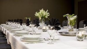 Una larga mesa de comedor vestida con manteles blancos, platos, copas y servilletas negras.