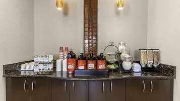 Un área de desayuno de hotel con una estación de café, una estación de té y una variedad de alimentos.