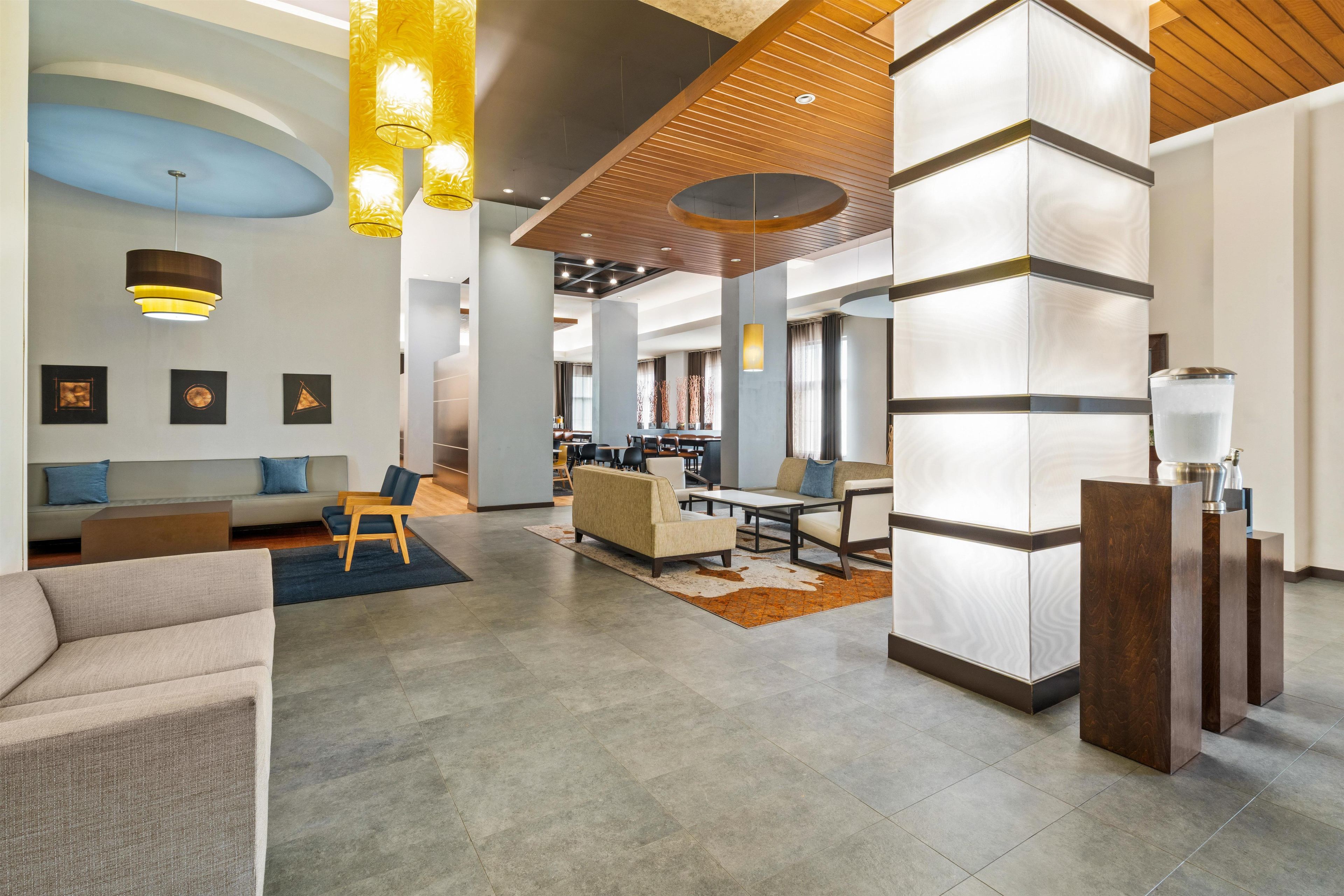 Eine geräumige Lobby mit modernem Design, inklusive einer Sitzecke mit Sofas und Sesseln, einem Empfangsbereich und einem großen, offenen Raum mit hoher Decke und Holzbalken.