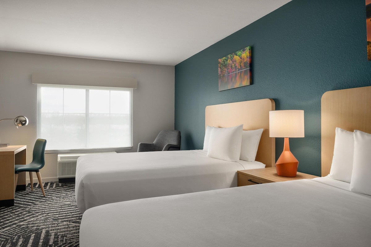 Une chambre d’hôtel avec deux lits, un bureau, une chaise et une fenêtre.