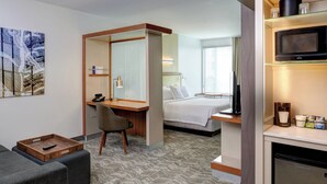 A hotel room with a bed, a desk, a chair, a sofa, a microwave, a refrigerator, and a painting on the wall. - SpringHill Suites by Marriott Saginaw (Saginaw)