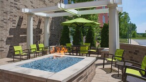 An outdoor patio with a fire feature, green chairs, and a covered seating area. - SpringHill Suites by Marriott Saginaw (Saginaw)